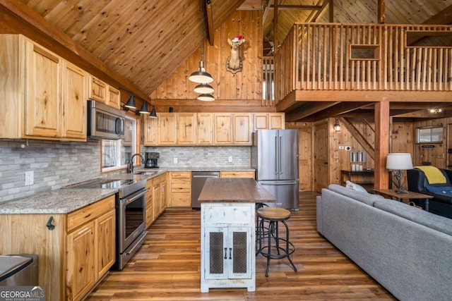 kitchen featuring open floor plan, a breakfast bar area, wood walls, light brown cabinets, and appliances with stainless steel finishes