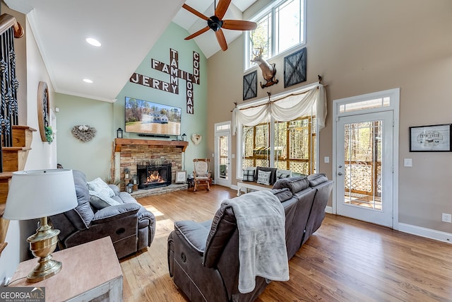 living area with wood finished floors, a stone fireplace, a ceiling fan, baseboards, and high vaulted ceiling