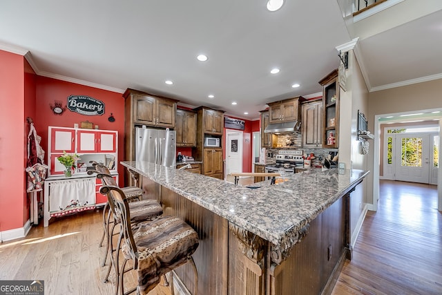 kitchen with stainless steel appliances, baseboards, decorative backsplash, crown molding, and under cabinet range hood