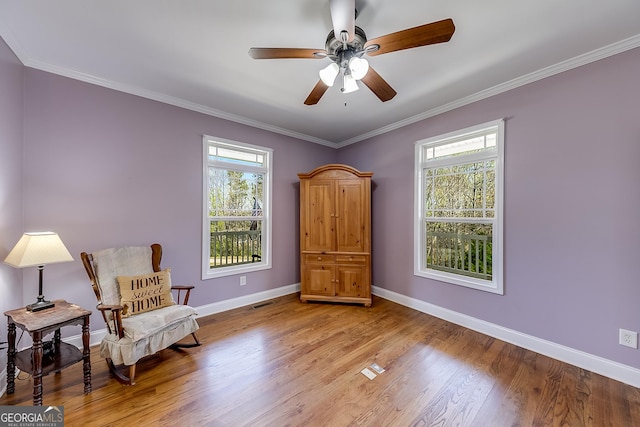 living area with wood finished floors, visible vents, a ceiling fan, ornamental molding, and baseboards