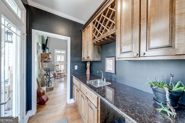 kitchen featuring crown molding, dark stone countertops, a sink, light wood-style flooring, and baseboards