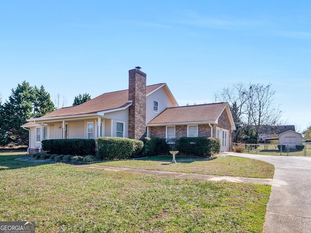 view of front of property featuring driveway, a chimney, brick siding, fence, and a front lawn