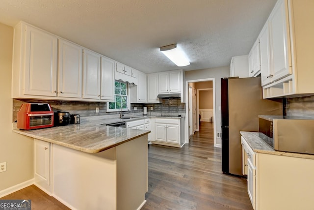 kitchen featuring a peninsula, a sink, a textured ceiling, stainless steel microwave, and under cabinet range hood