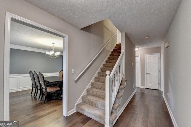 stairs with a textured ceiling, a notable chandelier, and wood finished floors