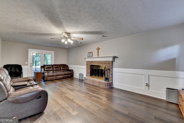 living area with a ceiling fan, a brick fireplace, a decorative wall, a wainscoted wall, and wood finished floors