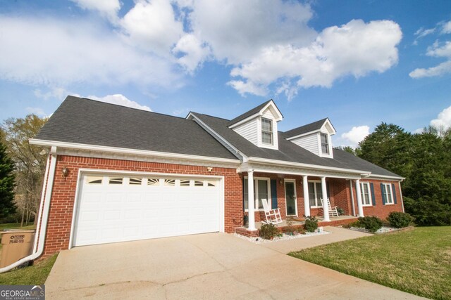 cape cod house with driveway, a front yard, brick siding, a porch, and a garage