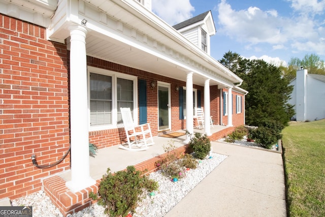 view of exterior entry with a porch and brick siding