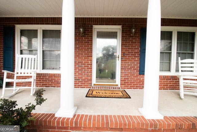 doorway to property featuring a porch and brick siding