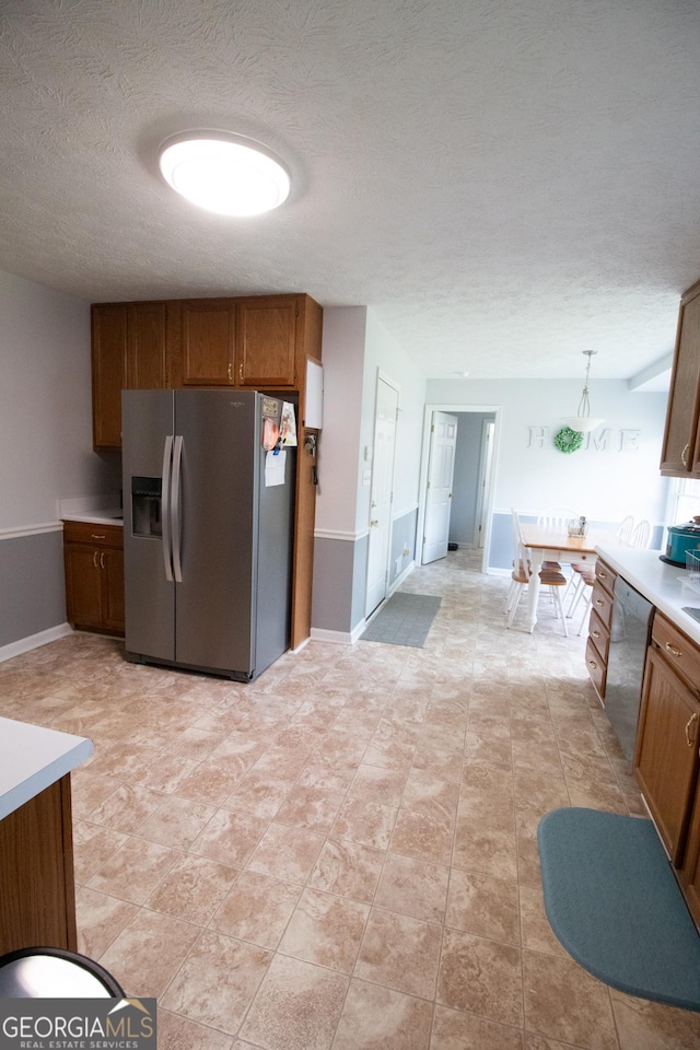 kitchen featuring a textured ceiling, light countertops, brown cabinets, appliances with stainless steel finishes, and decorative light fixtures
