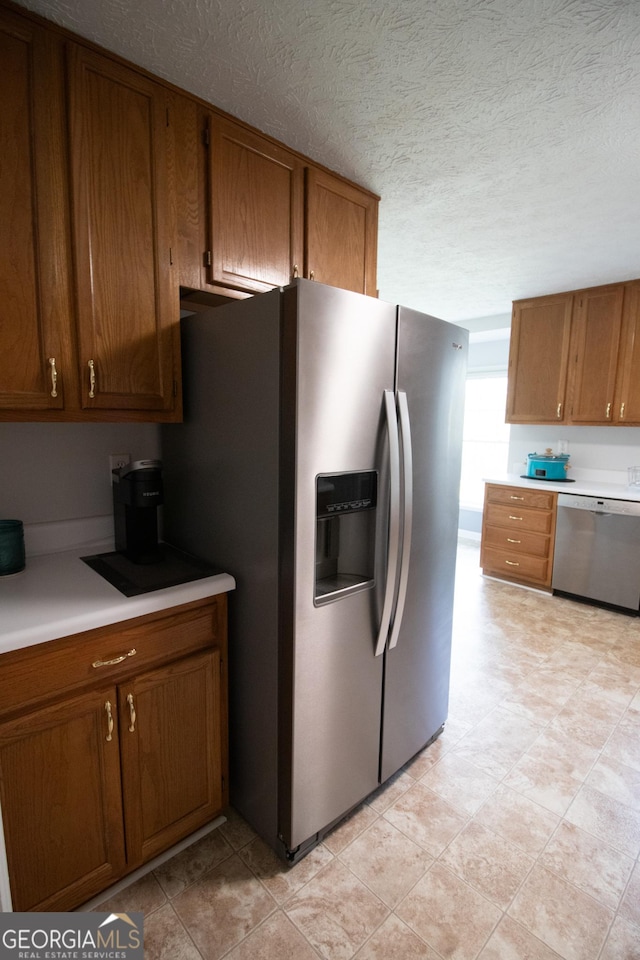 kitchen featuring a textured ceiling, light countertops, stainless steel appliances, and brown cabinetry