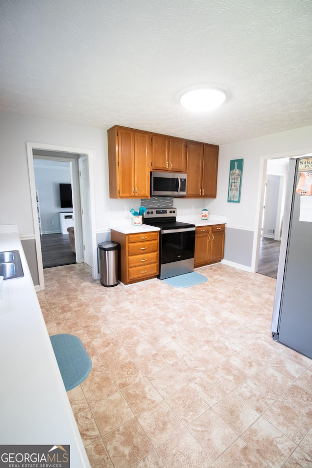 kitchen with light countertops, a sink, appliances with stainless steel finishes, and brown cabinets