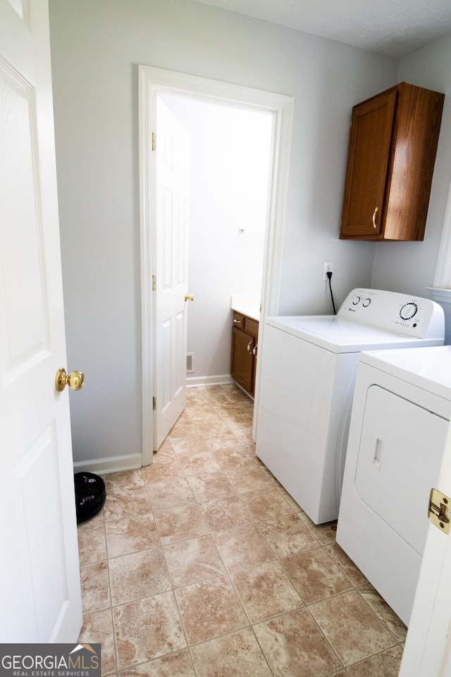 clothes washing area with washer and clothes dryer, cabinet space, and baseboards