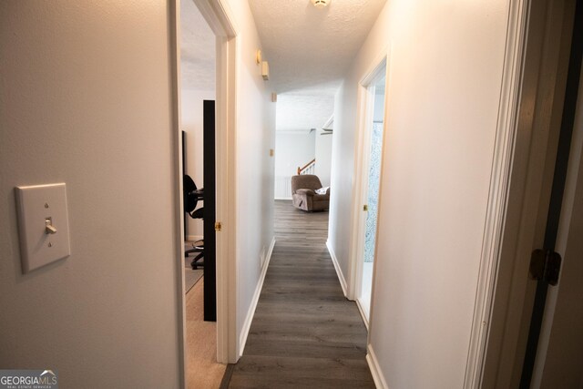 hall with dark wood-type flooring, baseboards, and a textured ceiling