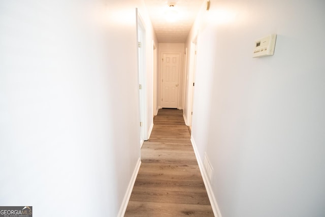hallway with baseboards, light wood-style floors, and visible vents