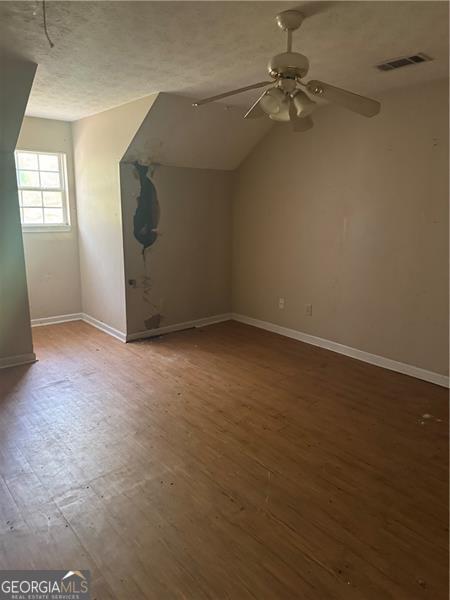 additional living space featuring baseboards, a textured ceiling, visible vents, a ceiling fan, and wood finished floors