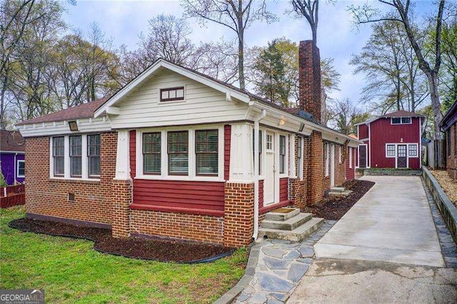 bungalow-style home featuring brick siding, entry steps, driveway, and a chimney