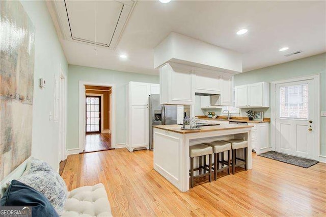 kitchen featuring a kitchen island, white cabinetry, butcher block countertops, a breakfast bar, and light wood-style floors