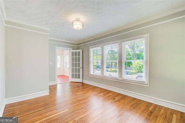 empty room with baseboards, crown molding, wood finished floors, and a textured ceiling