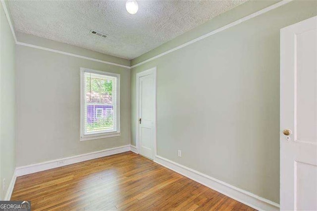 unfurnished room with baseboards, visible vents, a textured ceiling, and wood finished floors