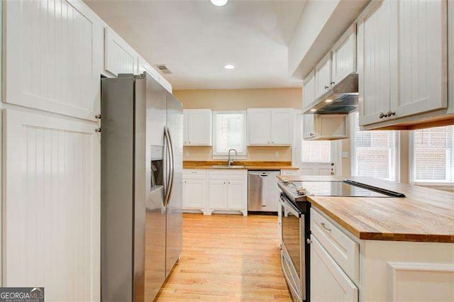 kitchen featuring stainless steel appliances, under cabinet range hood, white cabinetry, a sink, and light wood-style floors