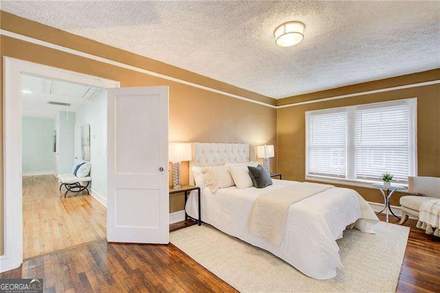 bedroom featuring baseboards, a textured ceiling, wood finished floors, and attic access