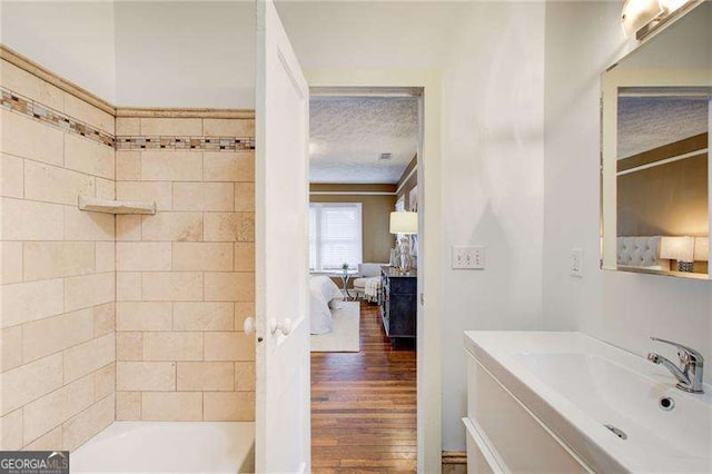 ensuite bathroom featuring bathtub / shower combination, vanity, wood finished floors, a textured ceiling, and ensuite bath