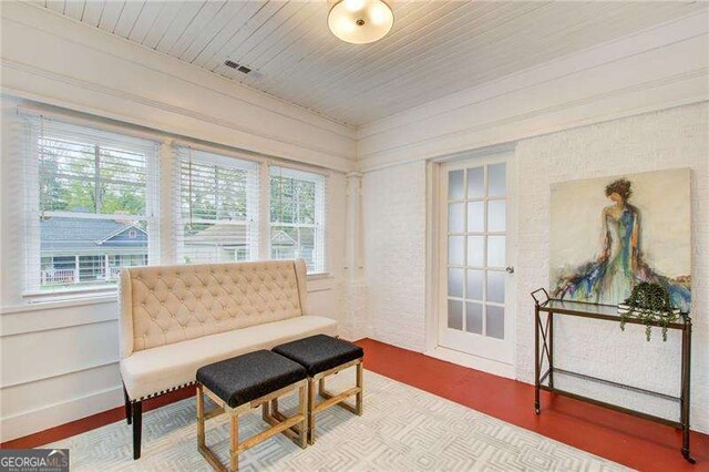 living area with a wealth of natural light, wooden ceiling, and brick wall