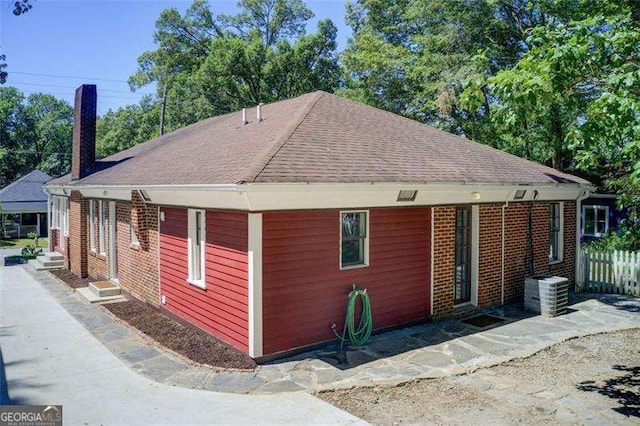 view of side of property featuring entry steps, fence, roof with shingles, and a chimney
