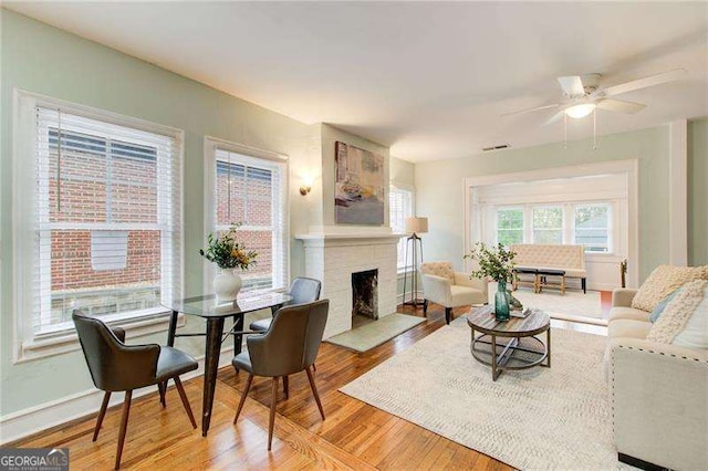 living area with a ceiling fan, light wood finished floors, a brick fireplace, baseboards, and visible vents