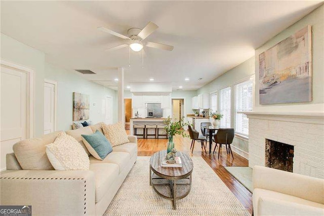 living area featuring a ceiling fan, light wood-style flooring, a fireplace, and visible vents