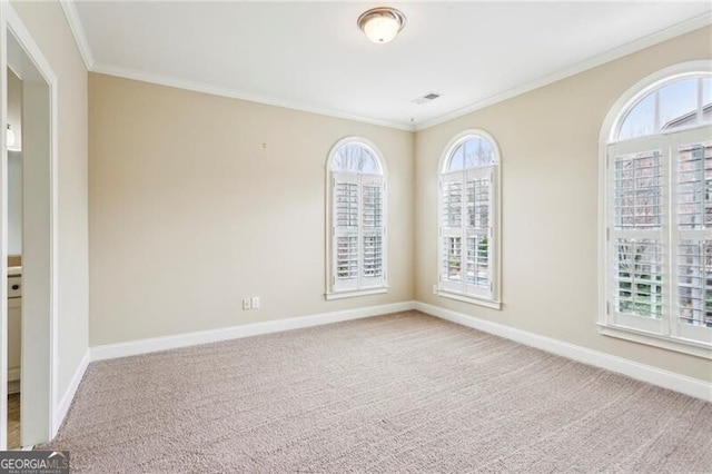 empty room with baseboards, visible vents, crown molding, and carpet
