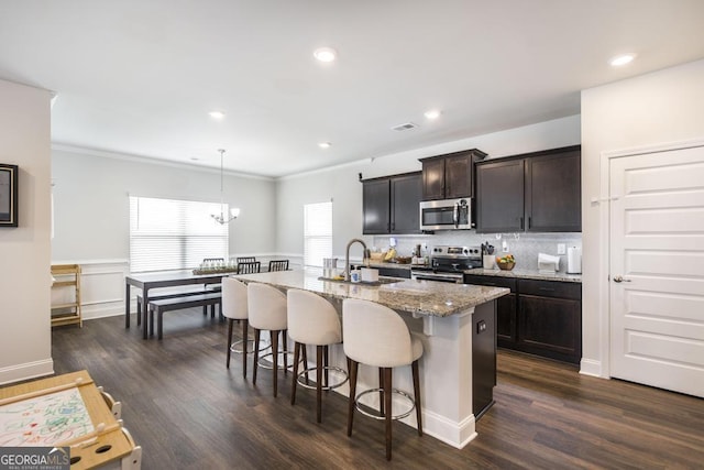 kitchen with an inviting chandelier, a sink, appliances with stainless steel finishes, light stone countertops, and a breakfast bar area