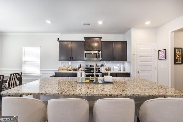 kitchen featuring backsplash, light stone counters, a kitchen bar, and stainless steel appliances