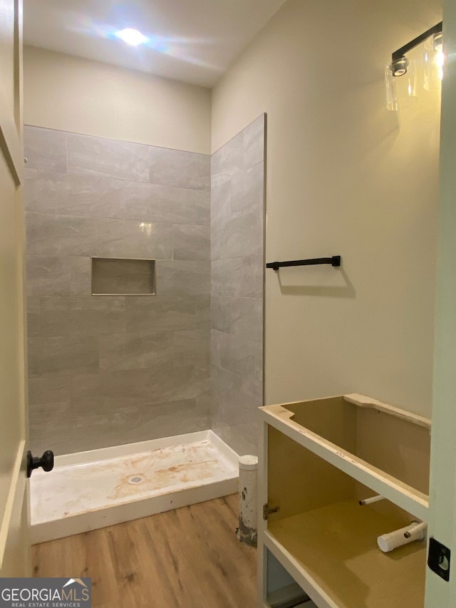 bathroom with wood finished floors and a tile shower