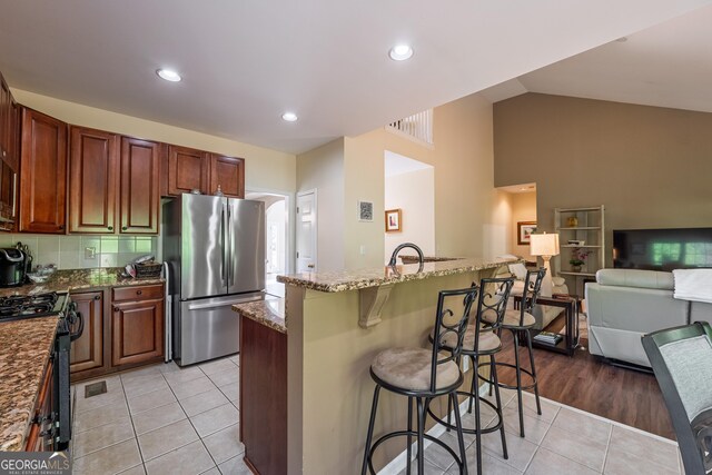 kitchen featuring light tile patterned flooring, open floor plan, a kitchen breakfast bar, dark stone counters, and stainless steel appliances