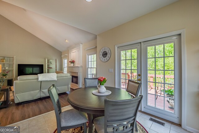 dining area with visible vents, a fireplace, light tile patterned flooring, and vaulted ceiling