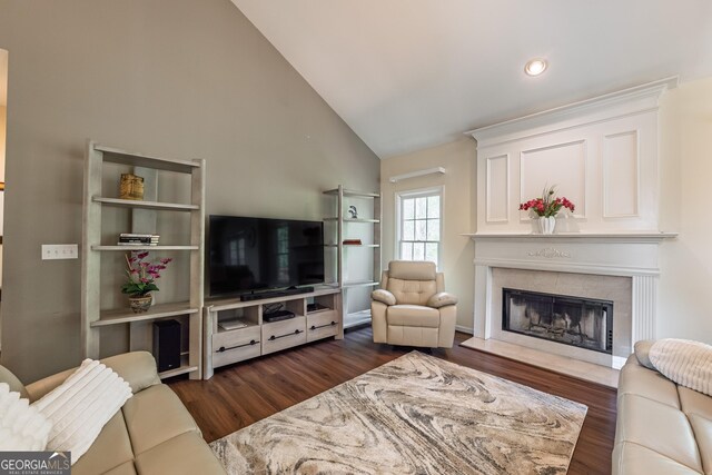 living room with a tiled fireplace, high vaulted ceiling, and dark wood-type flooring