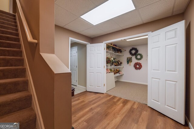 finished below grade area with a paneled ceiling, stairs, baseboards, and light wood-style flooring