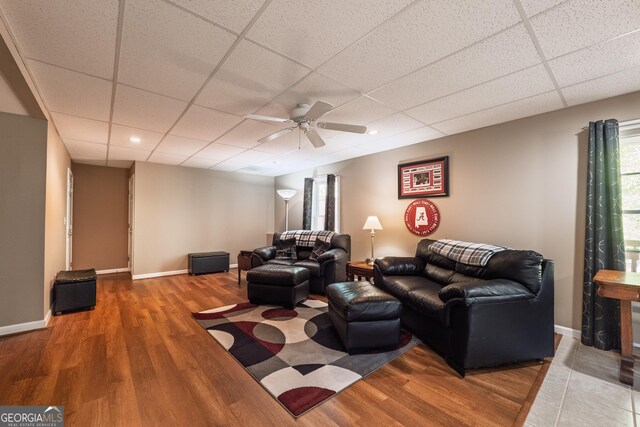 living area featuring baseboards, ceiling fan, a paneled ceiling, and wood finished floors