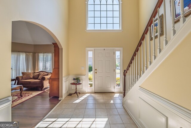 foyer featuring arched walkways, a high ceiling, a wealth of natural light, and a decorative wall