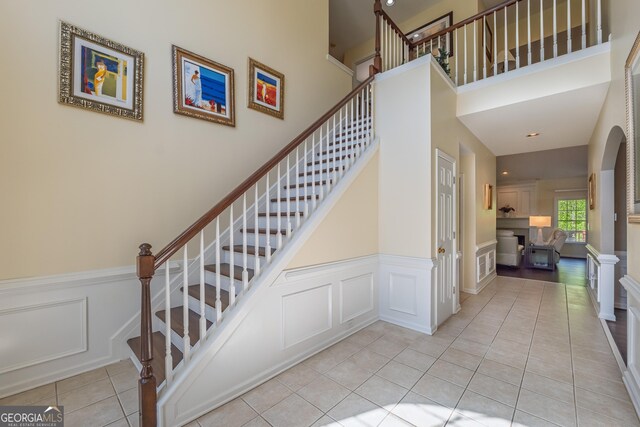 stairs featuring a high ceiling, tile patterned flooring, a decorative wall, a wainscoted wall, and visible vents