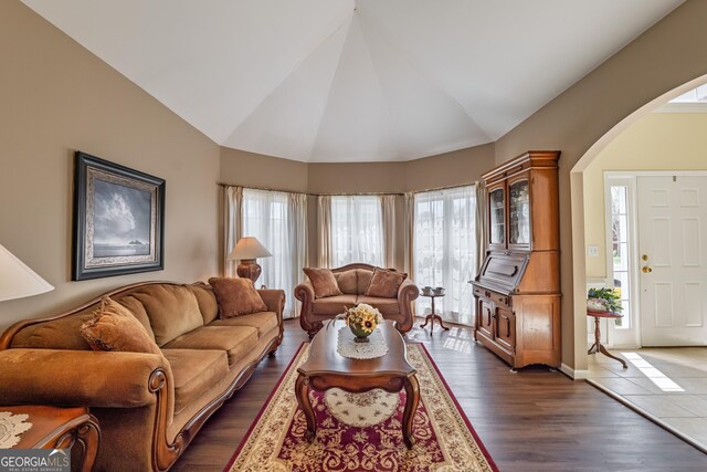 living room with arched walkways, vaulted ceiling, and dark wood-type flooring