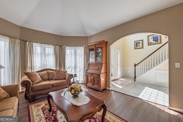 living room featuring arched walkways, wainscoting, vaulted ceiling, light wood-type flooring, and stairway