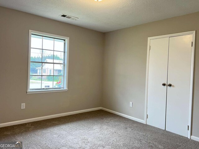 carpeted spare room with baseboards, a textured ceiling, and visible vents