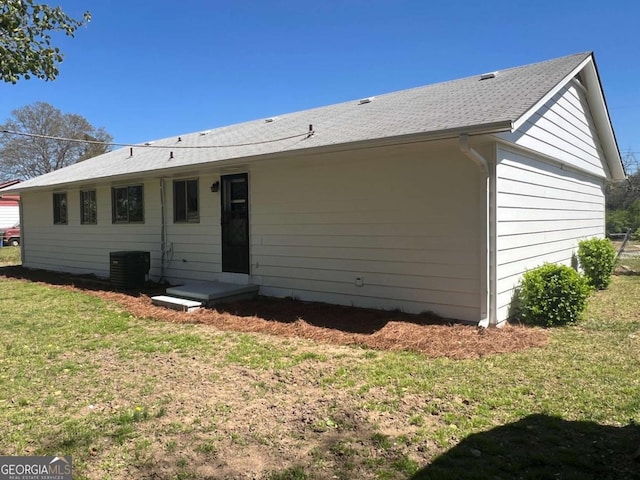 rear view of house with central AC unit and a yard