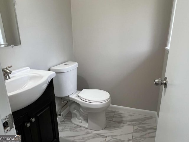 half bathroom featuring marble finish floor, baseboards, toilet, and vanity