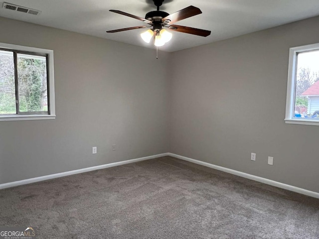carpeted spare room featuring a ceiling fan, plenty of natural light, baseboards, and visible vents