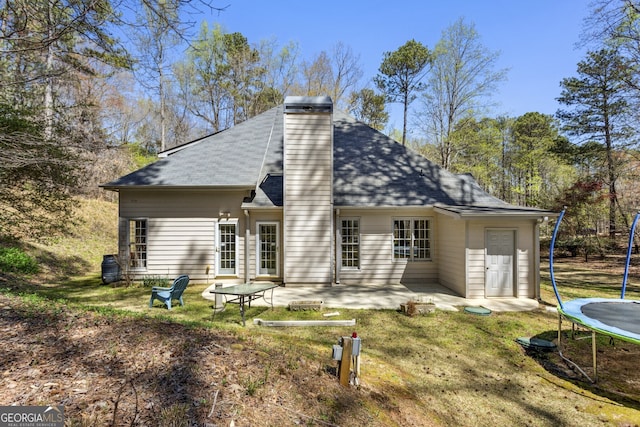 5163 Holly Springs Dr, Douglasville, GA 30135 - rear view of house with a patio, a chimney, a trampoline, roof with shingles, and a lawn