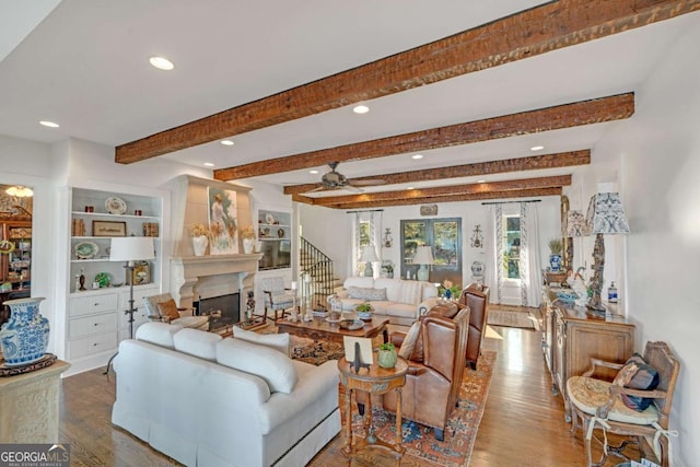 living room featuring a ceiling fan, beamed ceiling, a fireplace, and wood finished floors