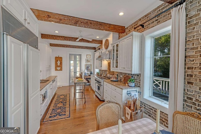 kitchen featuring range hood, brick wall, premium appliances, and white cabinetry